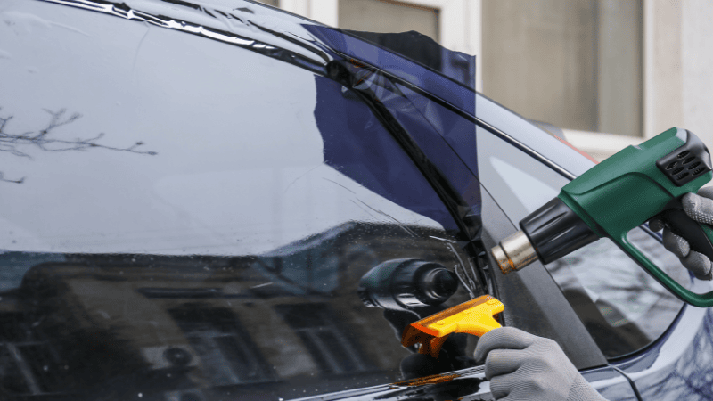 A man is installing a window tint film on the car with a heat gun.