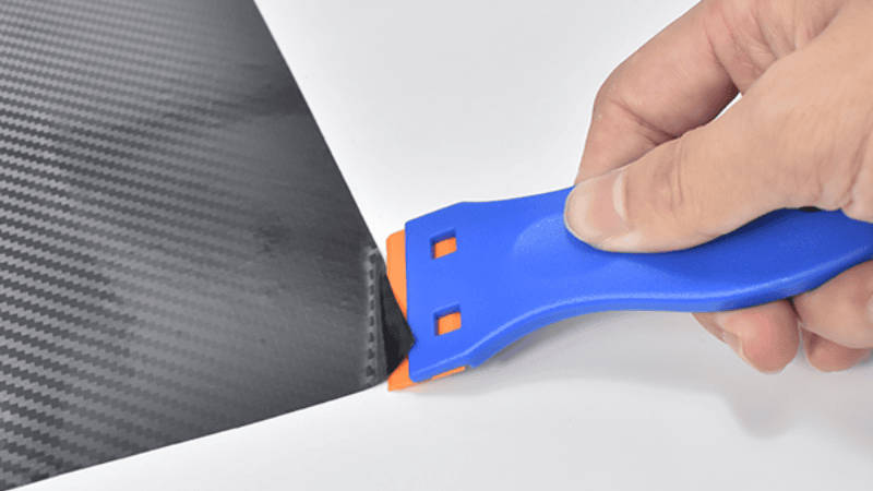A man is scraping the corner of the car film with a plastic scraper.