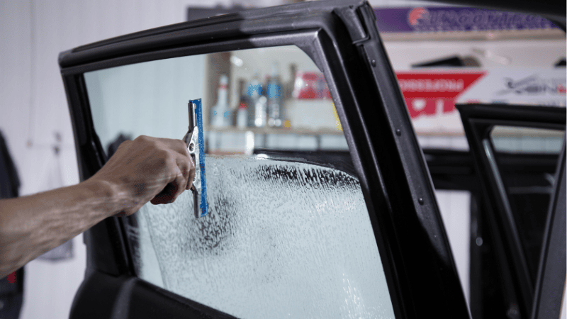 A man is washing the car Windows with a brush.