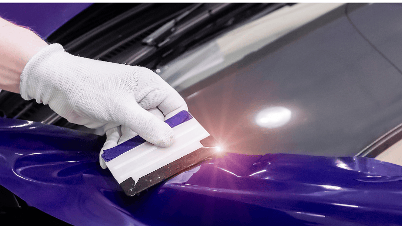 A man is installing car film with a plastic scraper.