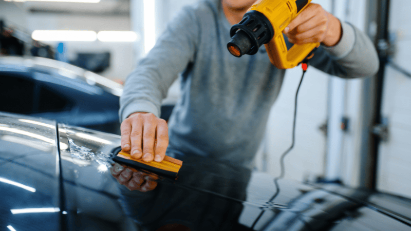 A man is using a heat gun to heat the car wrap.