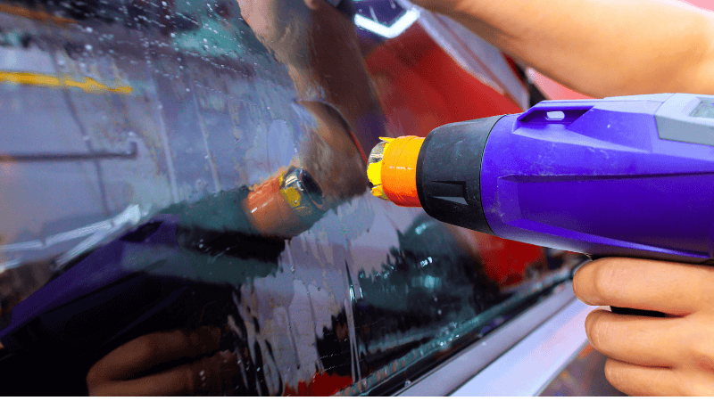 A man is using a heat gun on the car window.