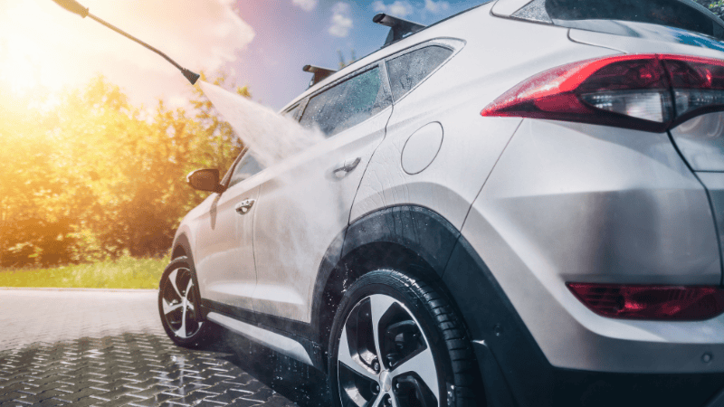 A man is washing the car with a high-pressure water jet.