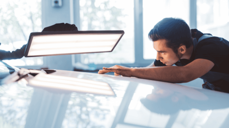 A man is inspecting the car's surface carefully.