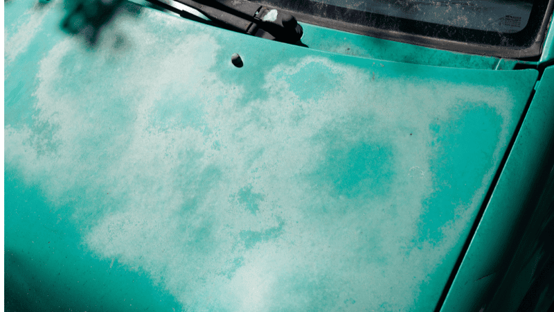 The paint on the hood of a green car has peeled off a lot.