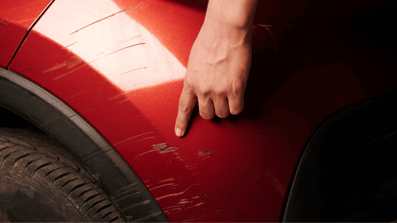 One finger is pointing at the scratches on the car.