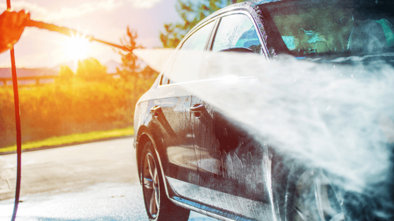 A man is washing the car with a high-pressure water jet.