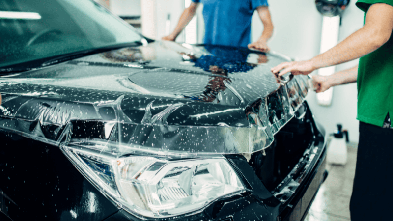 Two men are installing a PPF on the car.