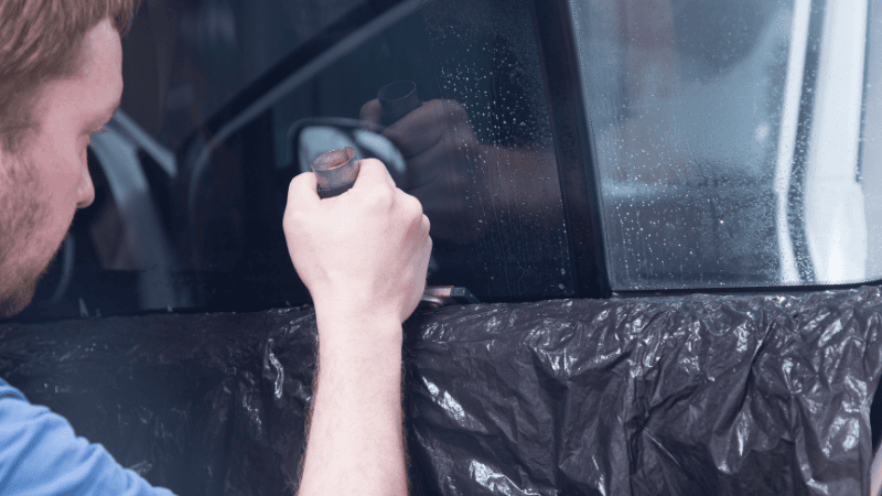 A man is installing a window tint film on the car.