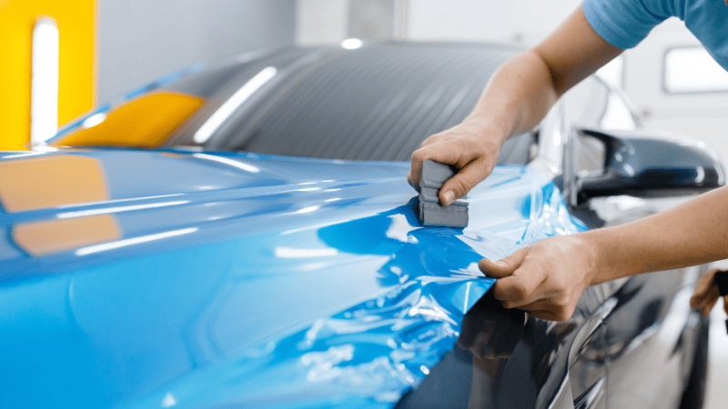 A man is applying a vinyl wrap on a car.
