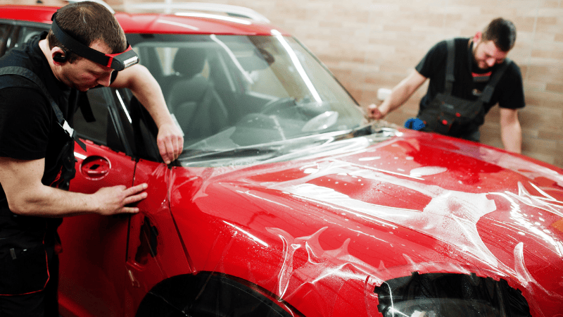 Two men are installing a PPF on a car.
