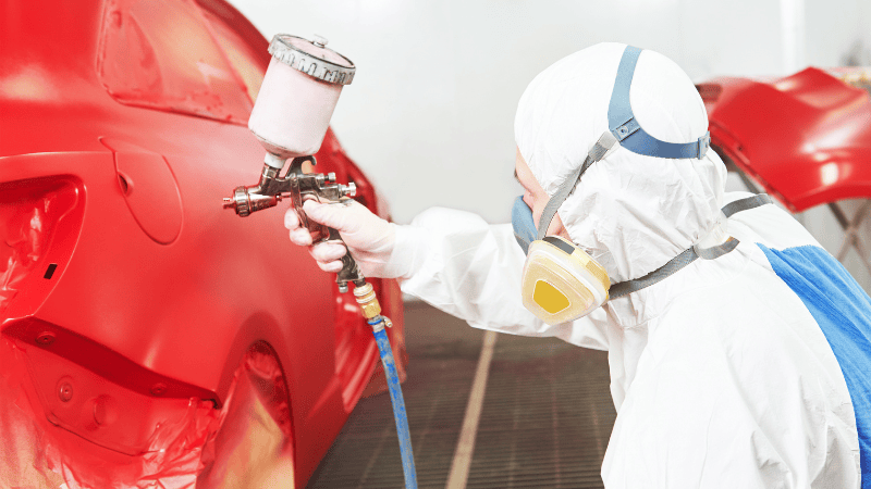 A man is painting a red car.