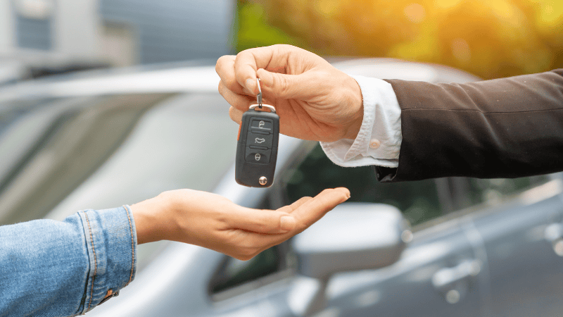 A man is giving a car key to a girl, selling the car.