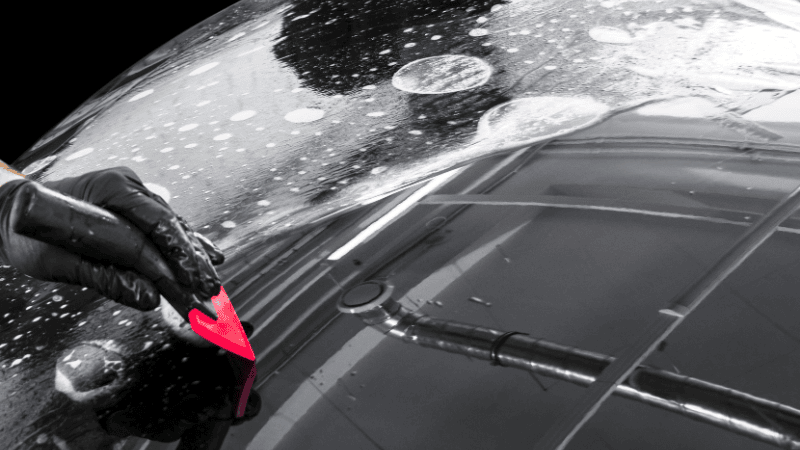 A man is installing a PPF on the car with a plastic scraper.