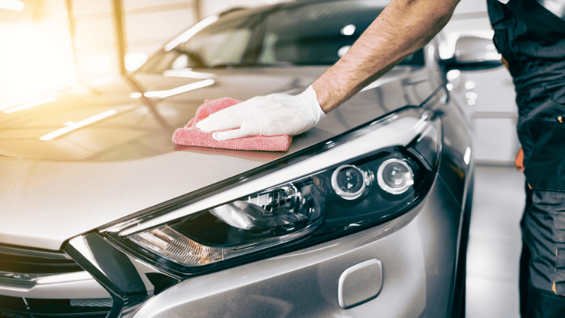 A man is wiping the car with a rag.