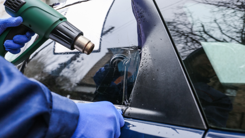 A man is heating the window tint with a heat gun.