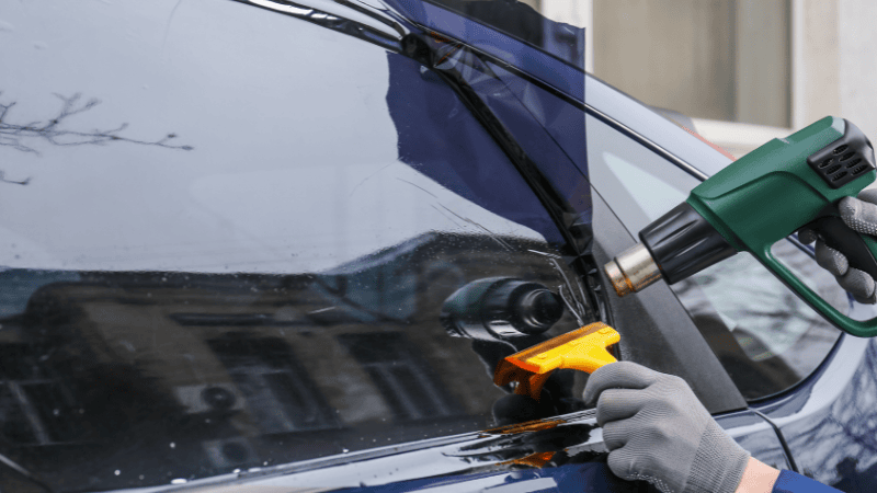 A man is installing a car window tint film with a heat gun.