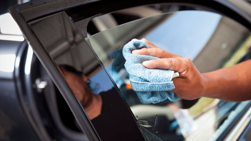 A man is cleaning the car window with a microfiber cloth.