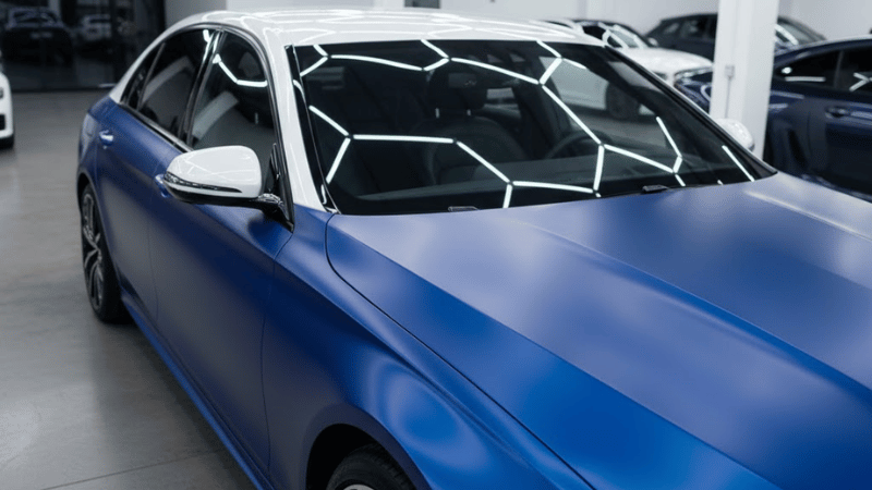 A car is featuring a sleek blue satin vinyl wrap on its body, beautifully contrasted with a chrome white wrap on the roof.