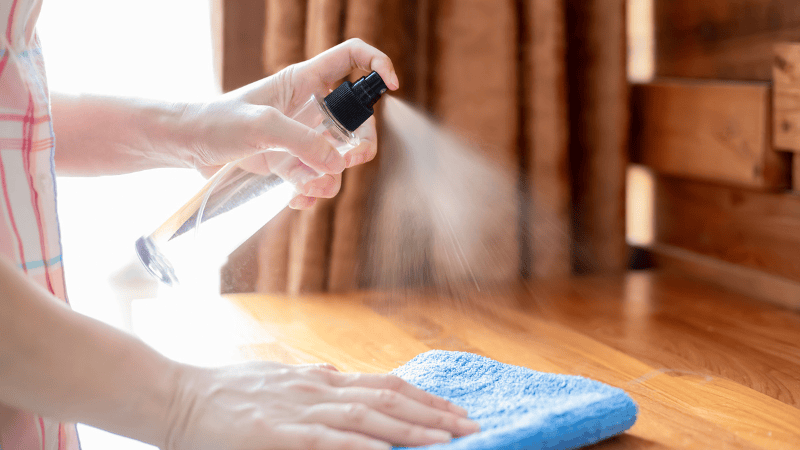 A woman is spraying rubbing alcohol on the table.
