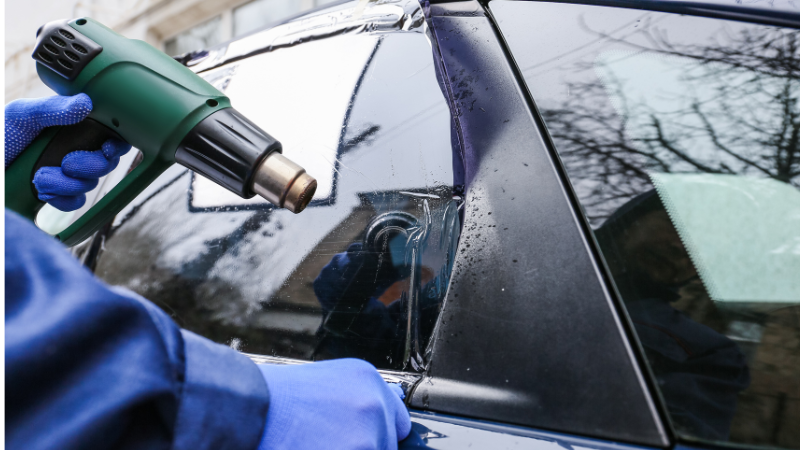 A man is installing the window tint film with a heat gun