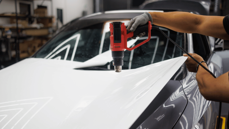 A man is applying the car wrap with a heat gun.